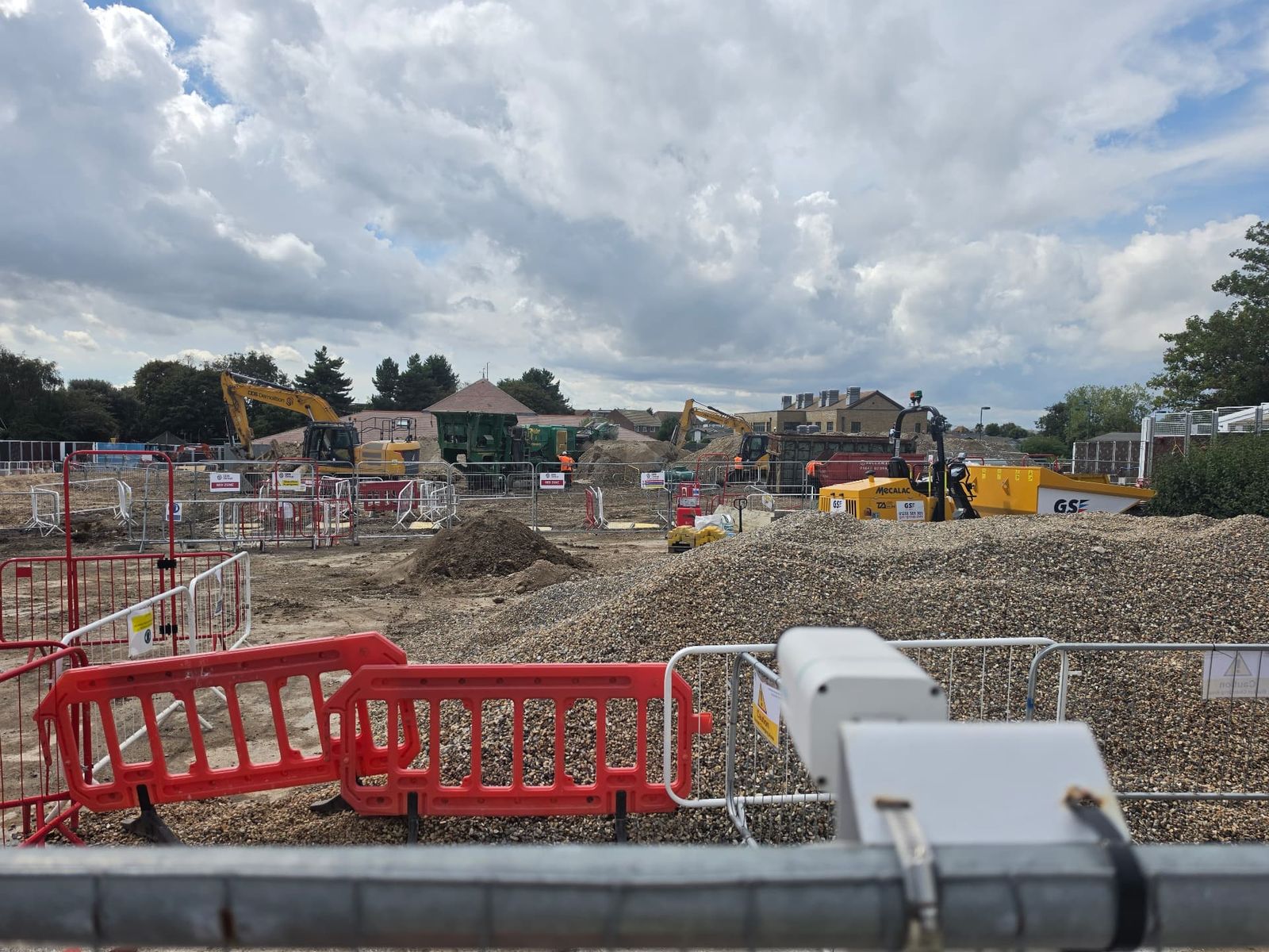 Active construction site with excavators, dumpers and aggregate stockpiles alongside nearby housing